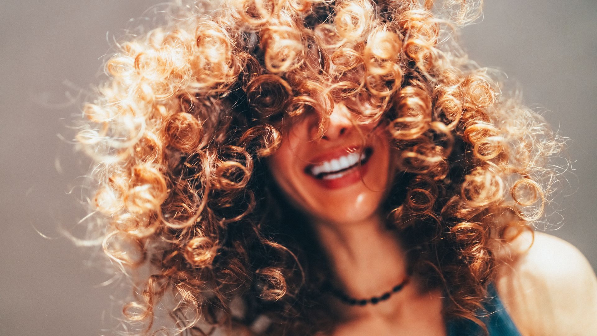 Femme souriante aux cheveux bouclés couvrant son visage.